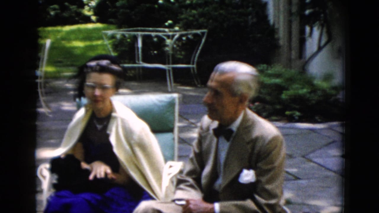 Older man in tan suit and bow tie converses with a bespectacled woman in a cream shawl on a stone garden patio, Washington DC area, circa 1952, 8mm home movie