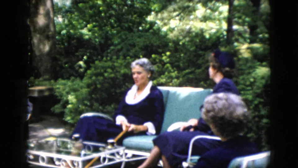 Older white-haired woman and companion in navy dresses seated outdoors, 8mm home movie, Washington DC area, circa 1952.