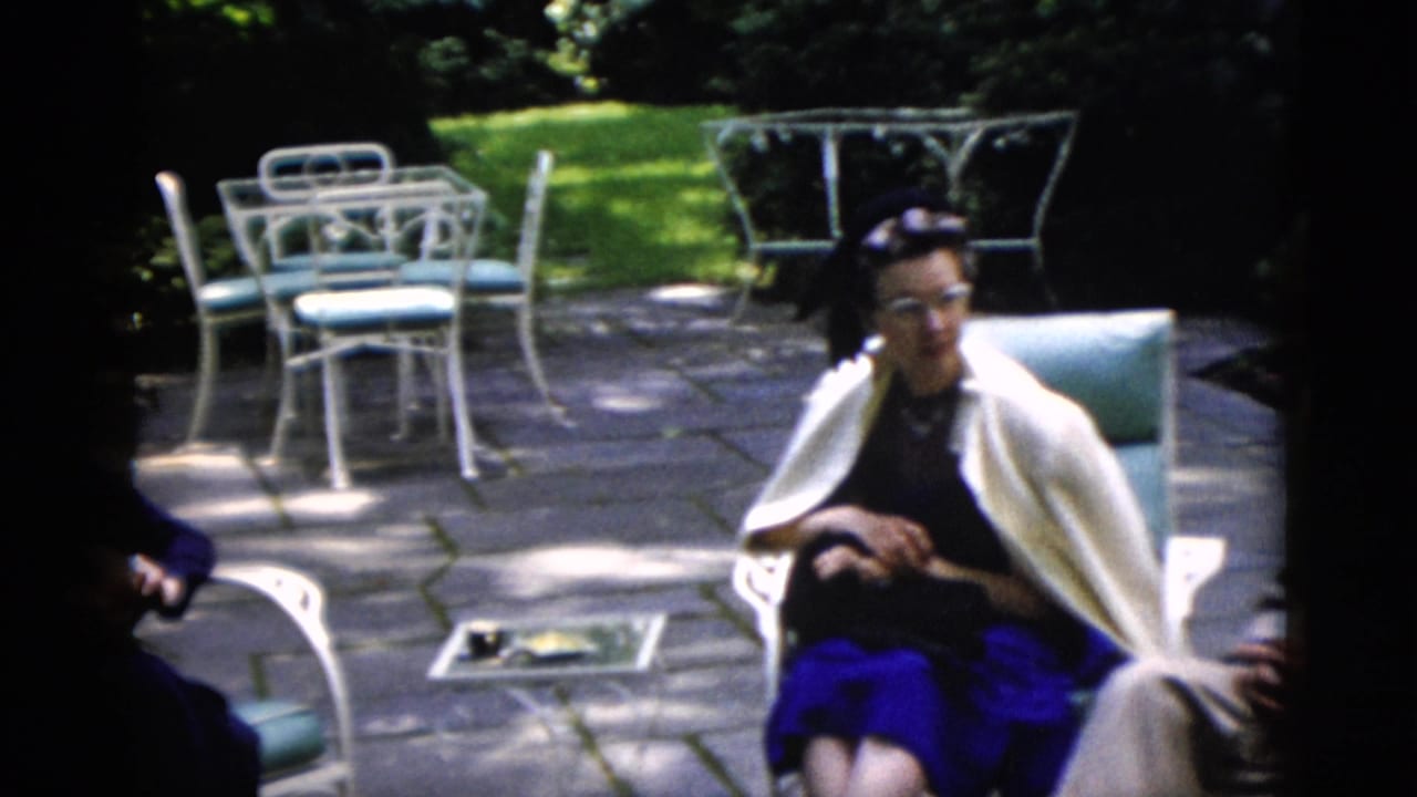 Older woman in a dark dress and white shawl sits on a sunlit patio in 1952 Washington, DC home-movie footage.