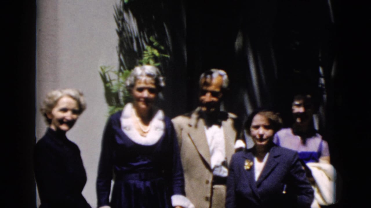 1952 Washington DC home-movie frame of formally dressed adults posing outdoors in sun and shadow near greenery.