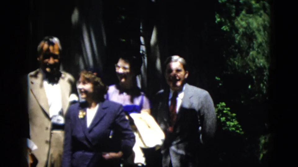 1952 Washington DC home-movie frame of adults in suits and dresses posing outdoors beside greenery and deep shade.