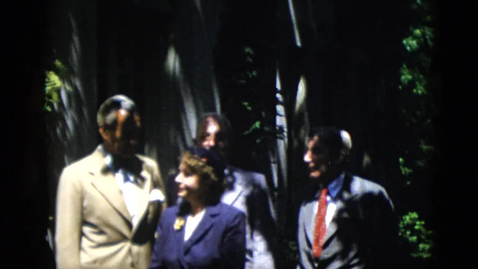 A man in a light suit, a woman in a dark suit, and a man with a red tie stand together in the 1952 Washington, DC home-movie scene.