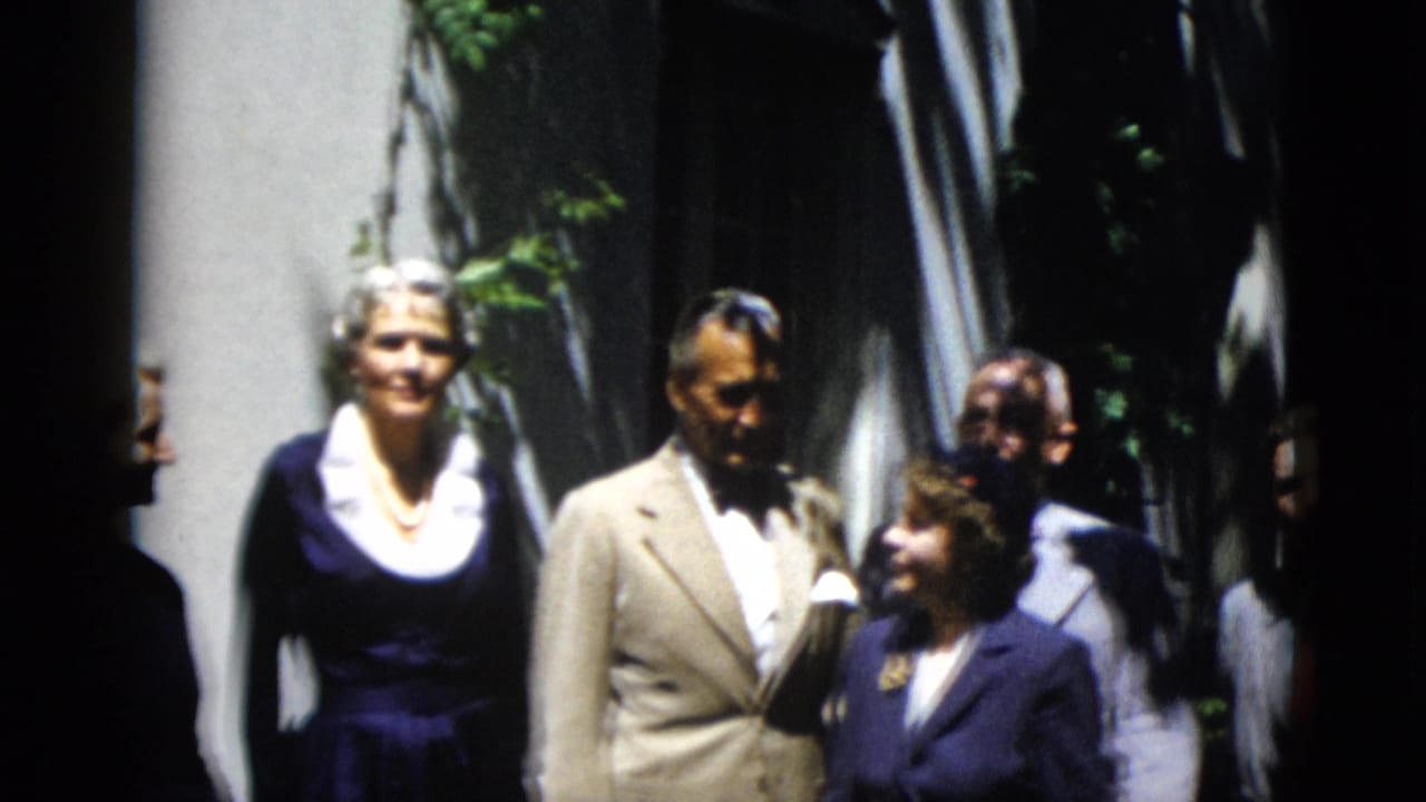 Adults in formal clothing pose together beside a sunlit doorway.