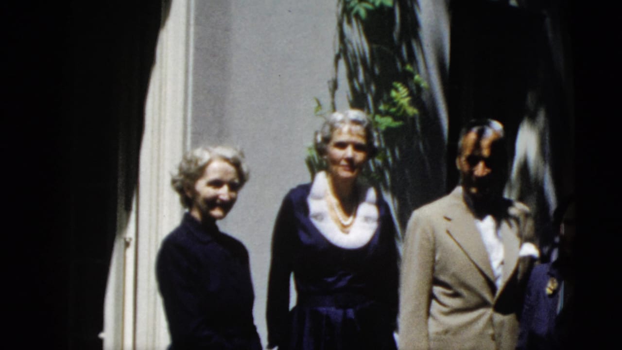 Three adults pose near a doorway with leafy shadows on the wall.