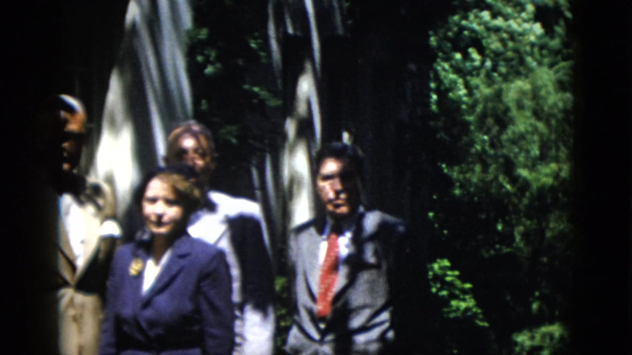 Adults in mid-century formal clothing stand in a Washington DC garden, partly obscured by shade and soft focus.