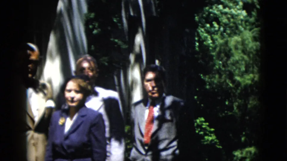 Adults in mid-century formal clothing stand in a Washington DC garden, partly obscured by shade and soft focus.