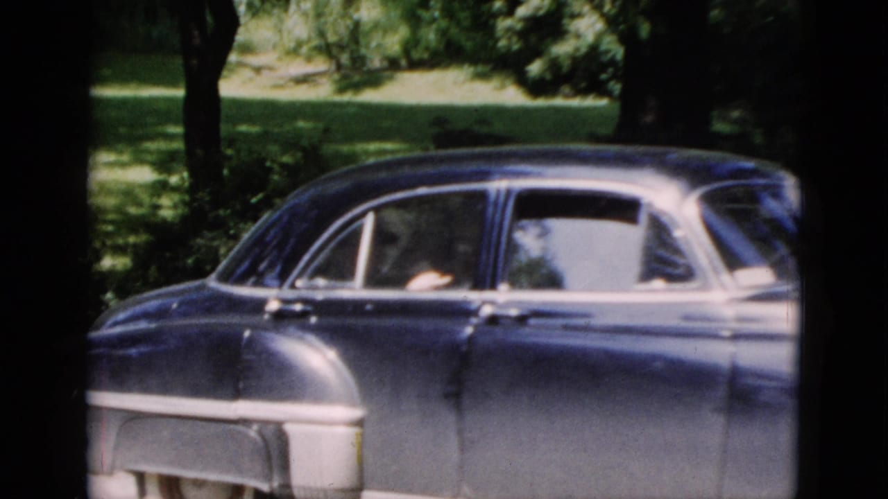 Side view of a dark blue mid-century sedan in Washington, DC, with at least one passenger visible through the open window.
