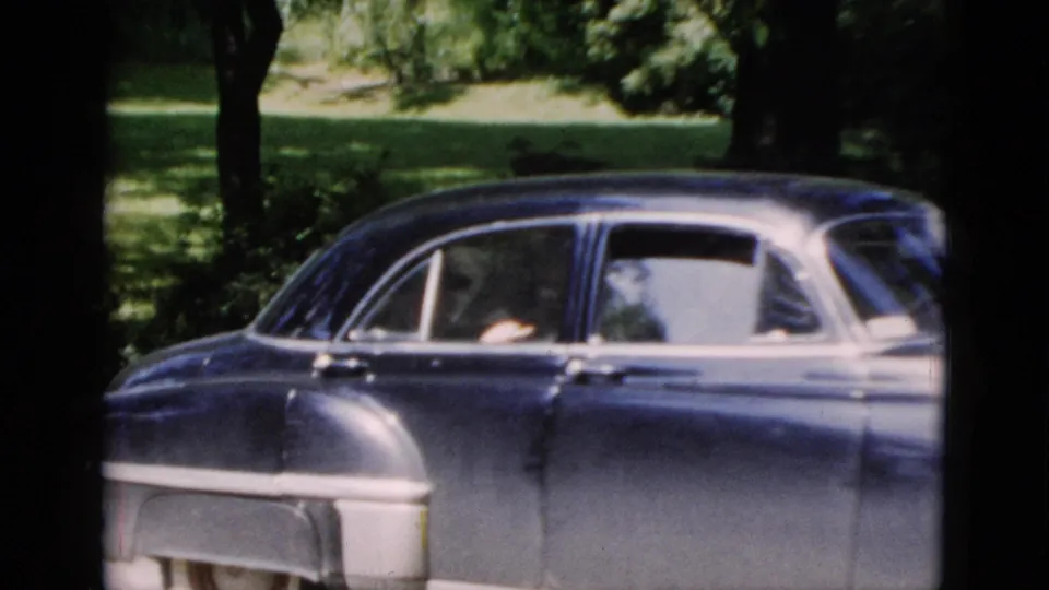 Side view of a dark blue mid-century sedan in Washington, DC, with at least one passenger visible through the open window.