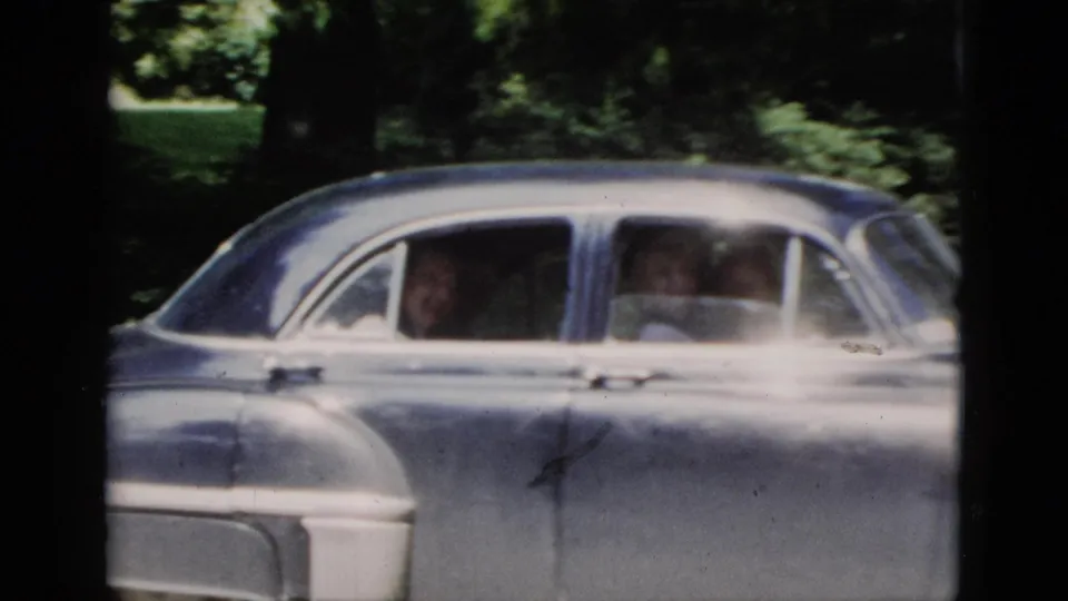 Final 1952 Washington, DC frame with two passengers visible through the sedan windows, surrounded by trees and lawn.