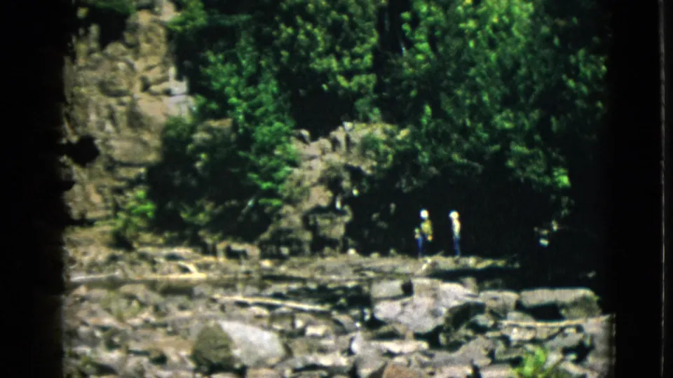 Distant visitors stand on a rocky riverbank amid dense Quebec forest in 1952 home-movie footage.