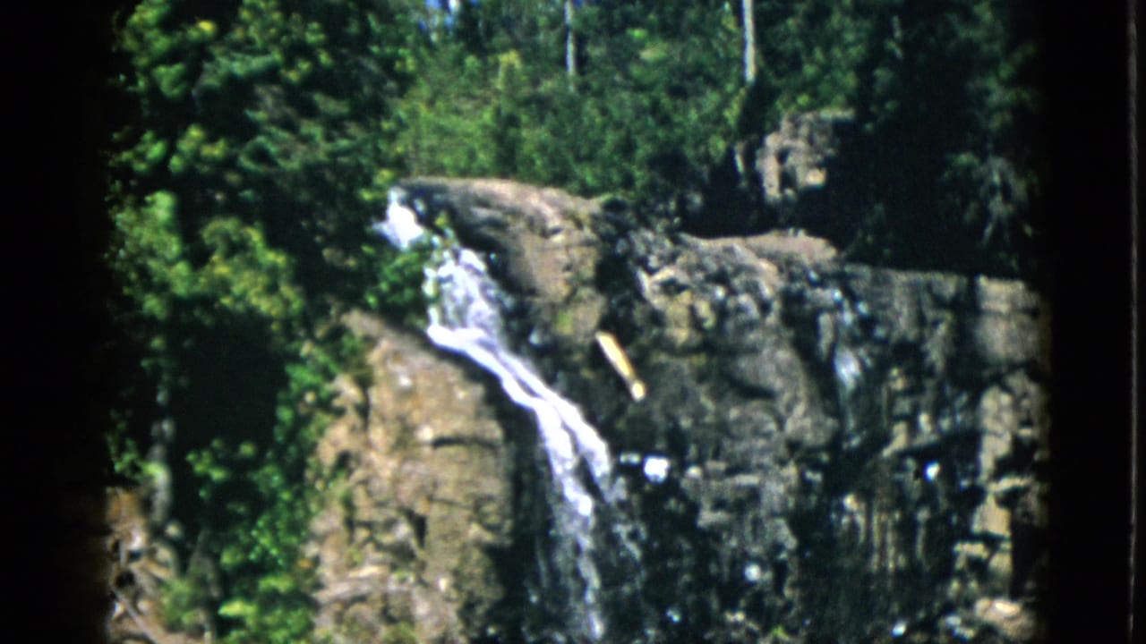 1952 Quebec 8mm frame showing white water descending over rugged brown rocks, bordered by trees and foliage.