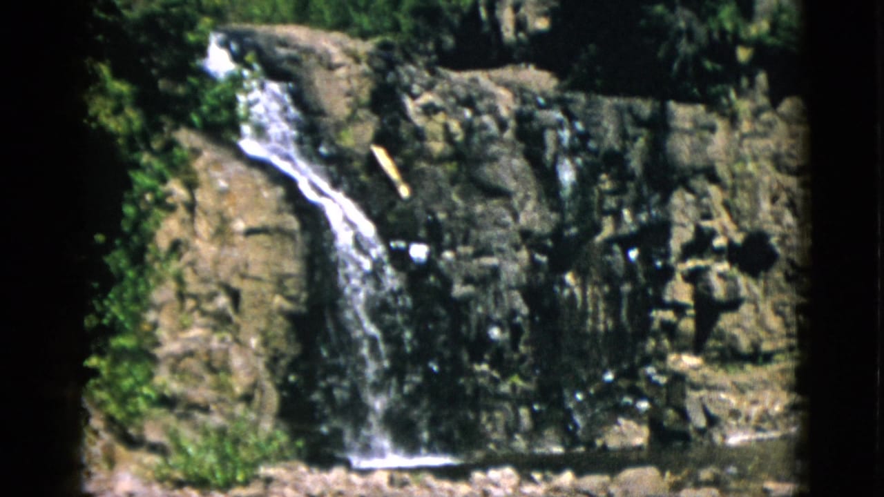1952 Quebec 8mm frame with the waterfall centered on a rugged cliff face and trees visible above the rocks.