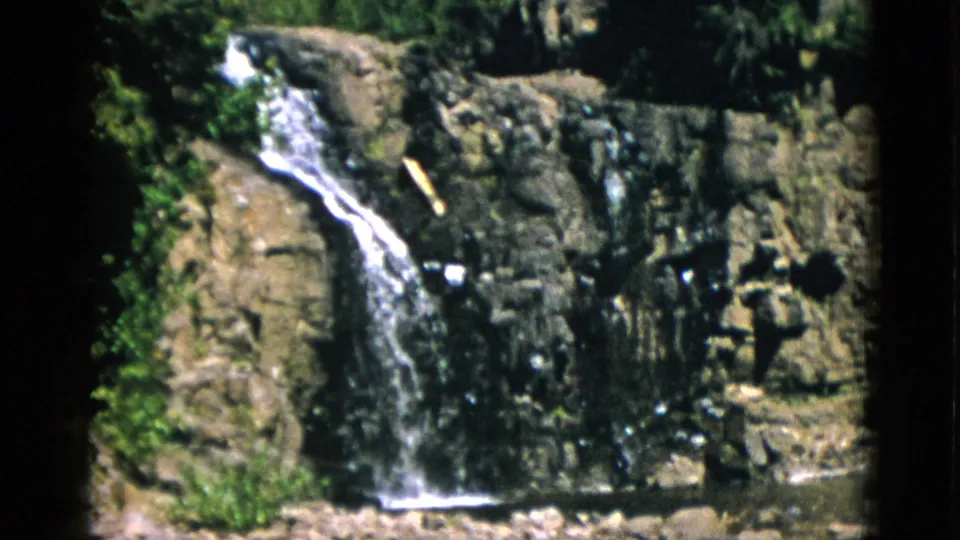 1952 Quebec 8mm frame with the waterfall centered on a rugged cliff face and trees visible above the rocks.