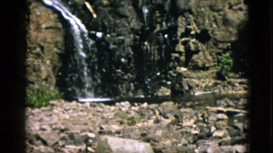1952 Quebec 8mm frame showing water reaching the base of the cliff beside a rocky stream bed and sparse greenery.