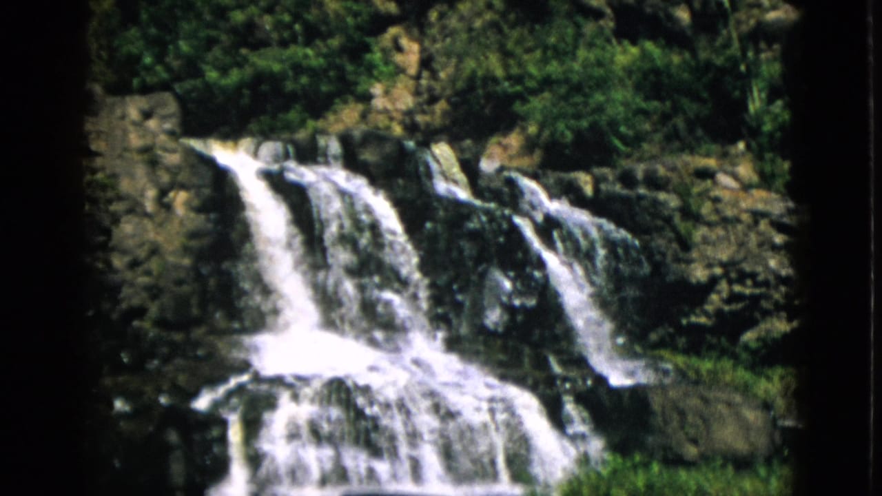 Multi-tiered waterfall over dark rocky ledges, Quebec Canada circa 1952, captured on 8mm home movie film with warm grain.