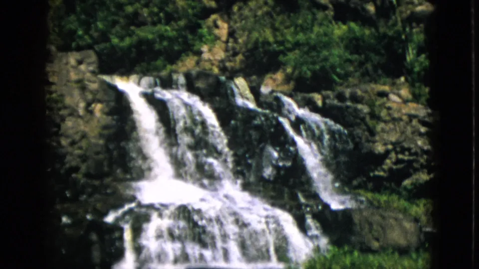 Multi-tiered waterfall over dark rocky ledges, Quebec Canada circa 1952, captured on 8mm home movie film with warm grain.