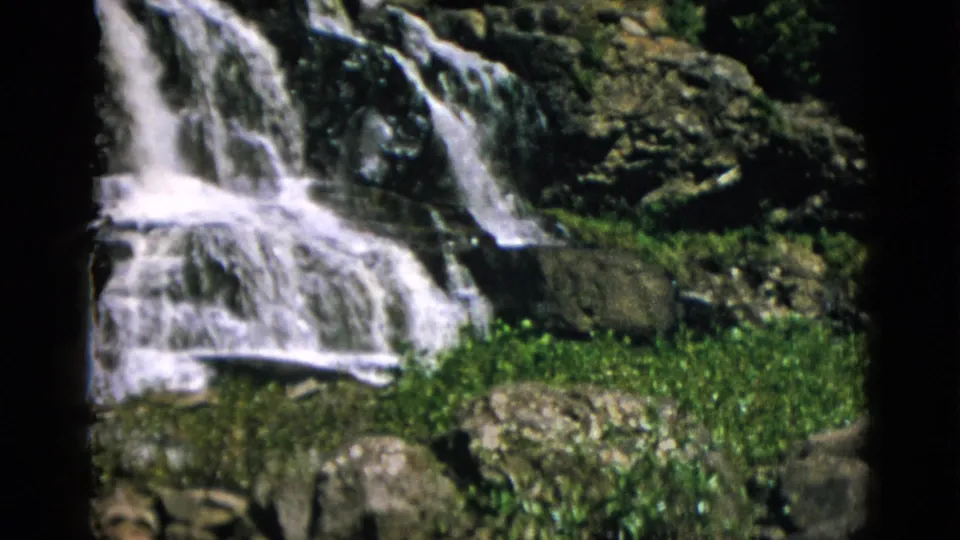 Wide view of waterfall over dark rocky tiers with green ground cover at base, Quebec Canada circa 1952, 8mm.