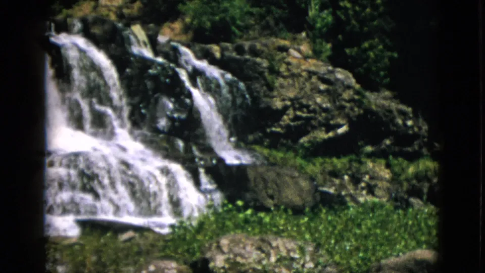 Waterfall descending over tiered dark rocks with green plants at base, Quebec Canada circa 1952, 8mm home movie.