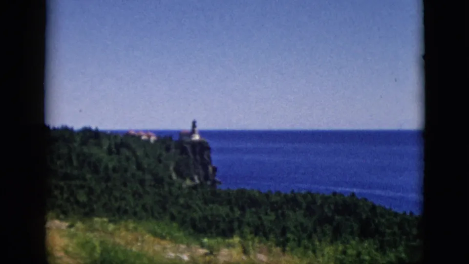 8mm pan continuing across lighthouse on forested cliff above large water body, c. 1952, attributed to Quebec, Canada.