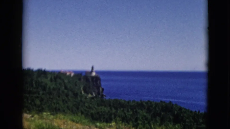 8mm frame widening to show more water and sky as lighthouse on cliff moves to lower left, c. 1952, Quebec, Canada.