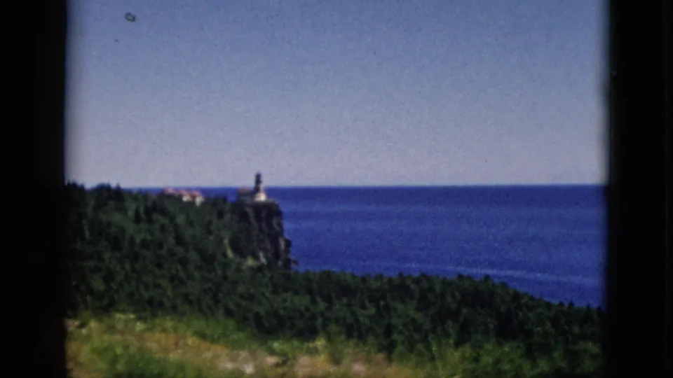 Final 8mm frame of coastal pan showing lighthouse headland at lower right with expansive water body, c. 1952, Quebec, Canada.
