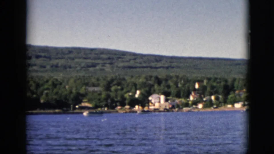 8mm color film, circa 1952, Quebec, Canada: lake surface, cluster of residential buildings at wooded shoreline, rolling hills in background.
