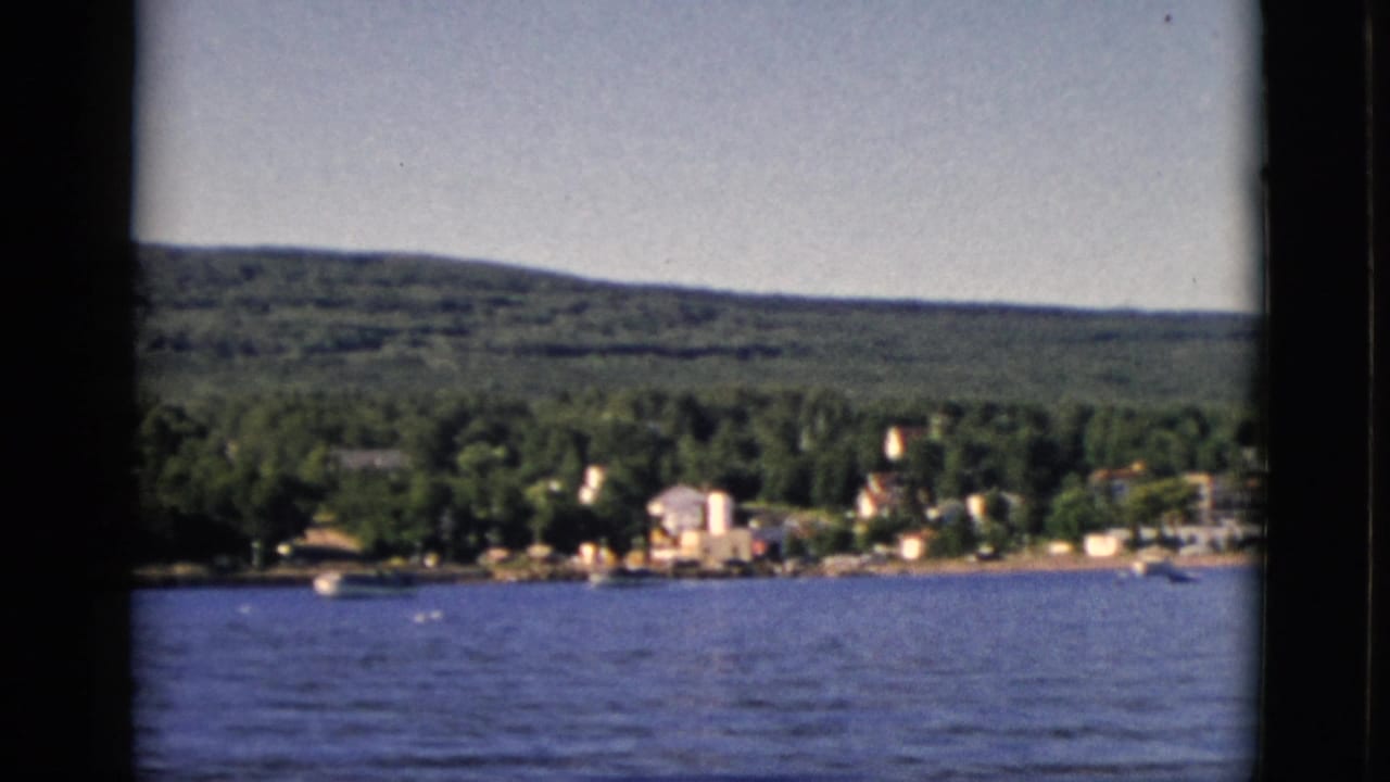 Calm lake with a small waterfront town and forested hills in the distance, filmed on 8mm.