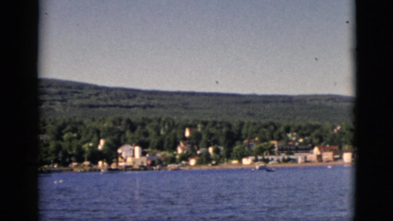8mm color footage of a small Quebec waterfront town seen across open water, with forested hills behind, circa 1952.