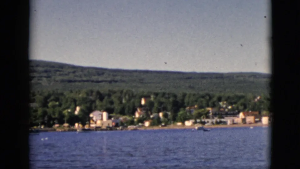 8mm color footage of a small Quebec waterfront town seen across open water, with forested hills behind, circa 1952.