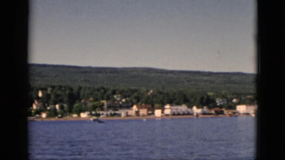 Final 8mm frame showing a wider sweep of the Quebec lakeside settlement, buildings spread along the waterfront with dense forest backdrop, circa 1952.