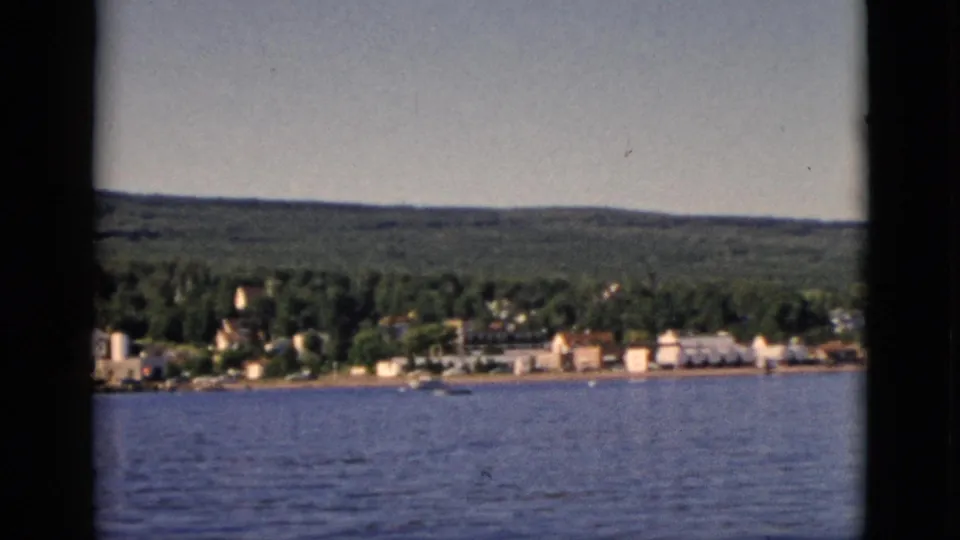 Wider 8mm view with expanded sky and open water; Quebec lakeside settlement visible along the treeline in the lower portion of the frame, circa 1952.