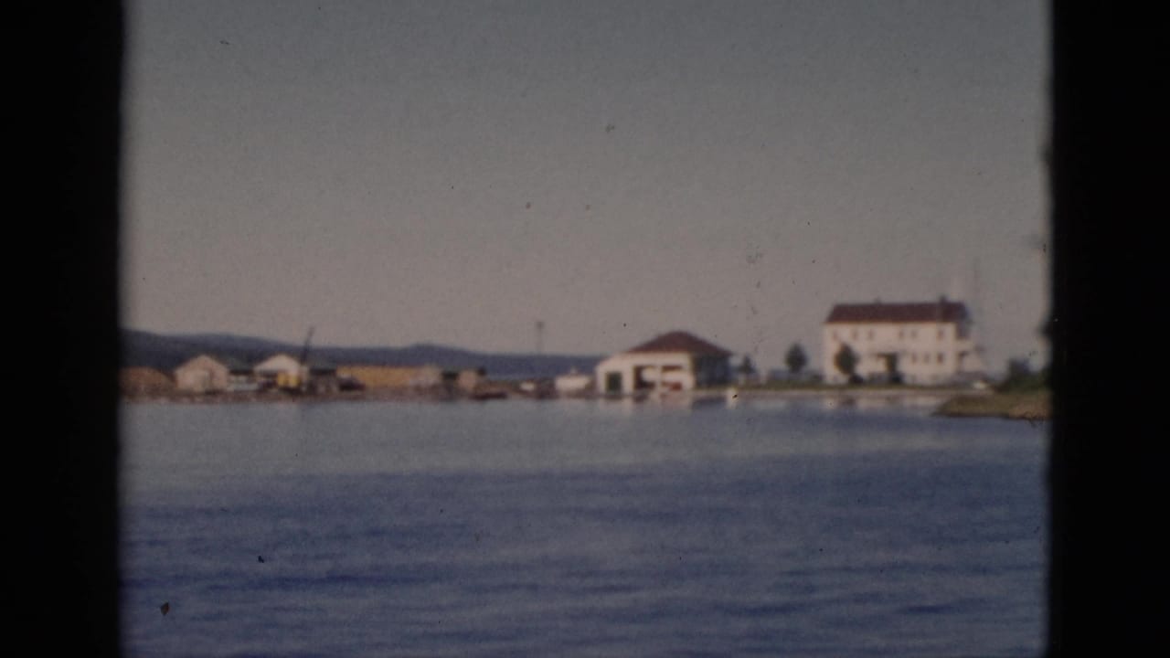 Boat-eye view of a Quebec lakeside waterfront with a white multi-story building and smaller structures on a distant shore.