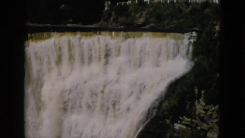 8mm footage c. 1952, Quebec, Canada: camera tilted down to reveal full height of cascading falls dropping into a rocky gorge with vegetation at the base.