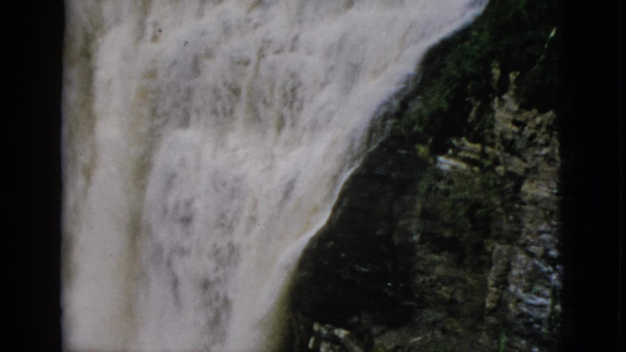 White turbulent water falls against dark rock with slight vegetation at frame right, 8mm home movie circa 1952, Quebec.