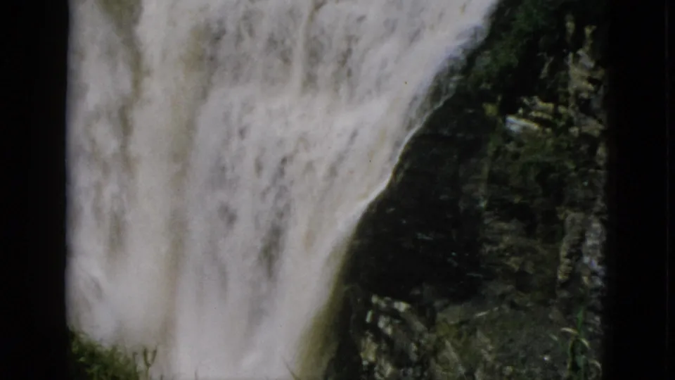 Turbulent white water flows over dark layered rock with rocky base formations visible below, 8mm home movie circa 1952, Quebec.