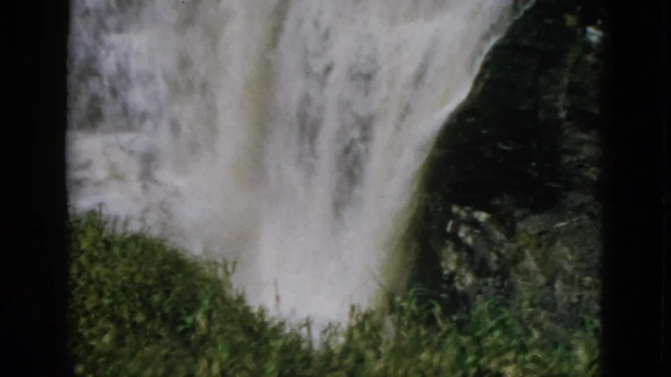 8mm home movie, circa 1952, Quebec Canada — waterfall cascading over dark rocky outcrop with bright green grassy mound in foreground