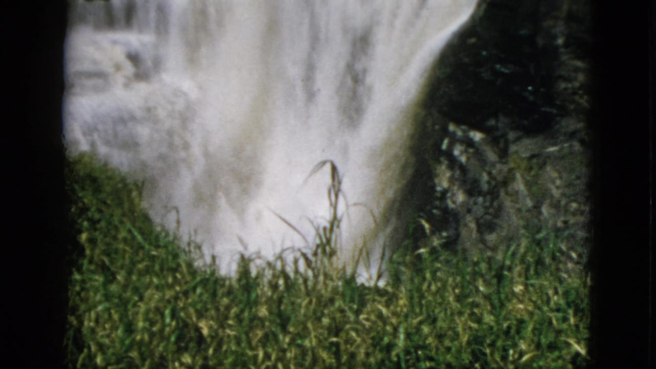 Close-up 8mm frame of a rushing waterfall with lush green reeds in the foreground, Quebec, Canada, circa 1952.