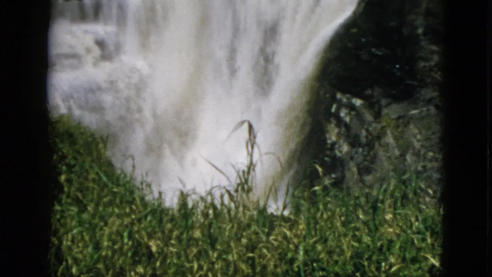 Close-up 8mm frame of a rushing waterfall with lush green reeds in the foreground, Quebec, Canada, circa 1952.