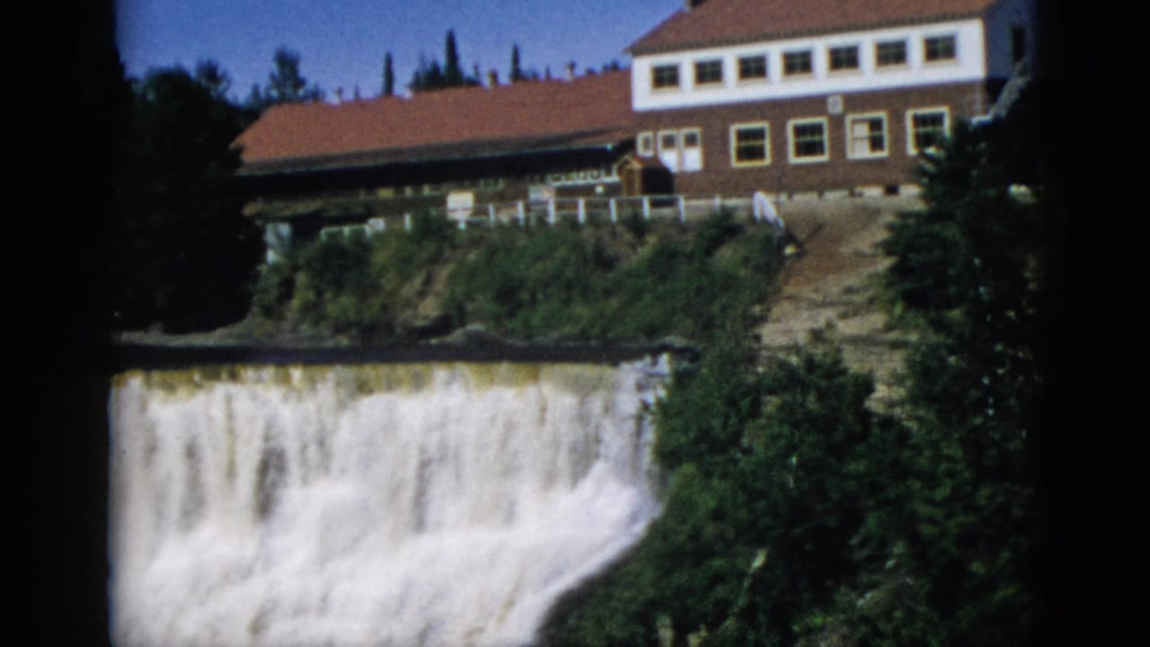 Camera pan reveals a large brick-and-white hotel with red tiled roof above a wide waterfall; Quebec, Canada, circa 1952 8mm footage.