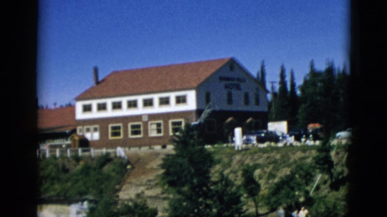 Exterior of a two-story hotel with red-tiled roof on a rocky wooded cliff above a waterfall gorge, Quebec Canada circa 1952, 8mm home movie frame.