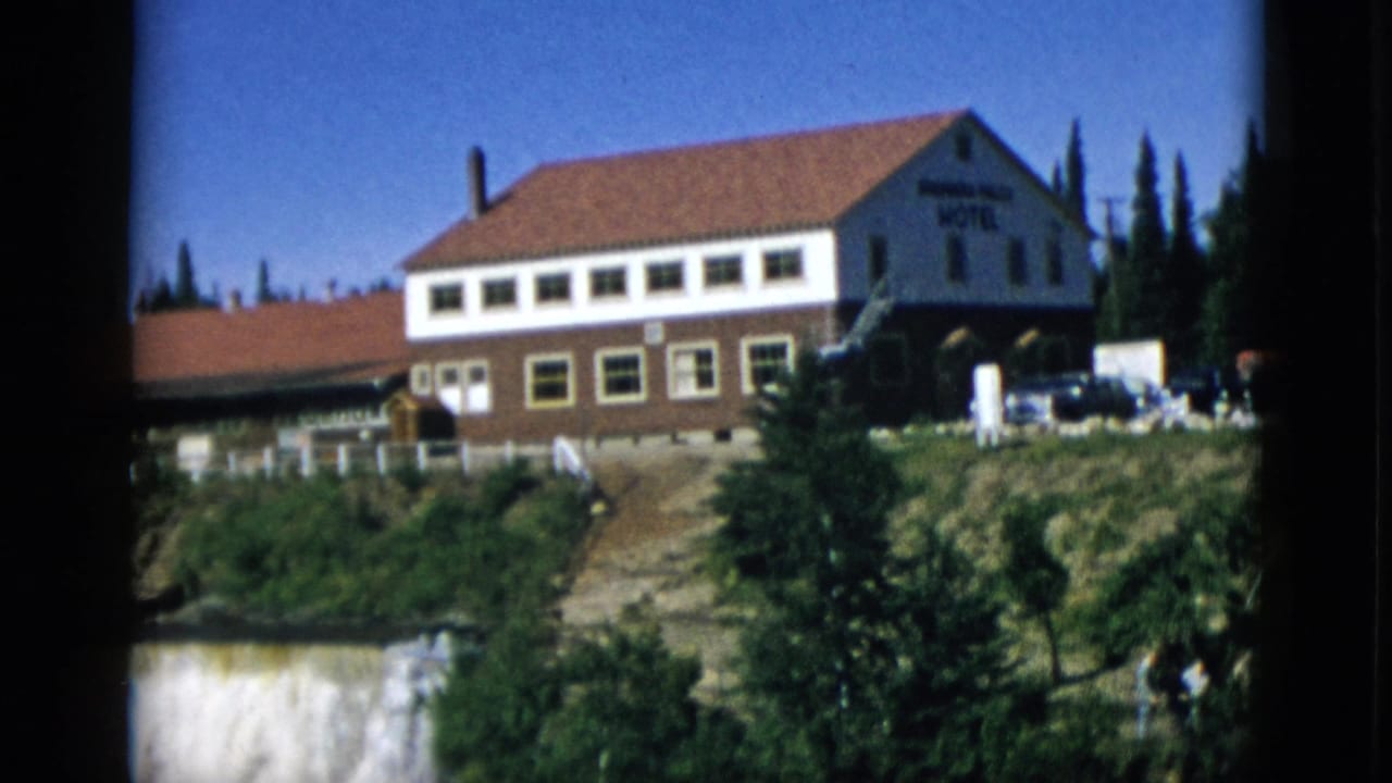 Hotel on wooded cliff with pan beginning to reveal waterfall cascade at right edge, 8mm film still.
