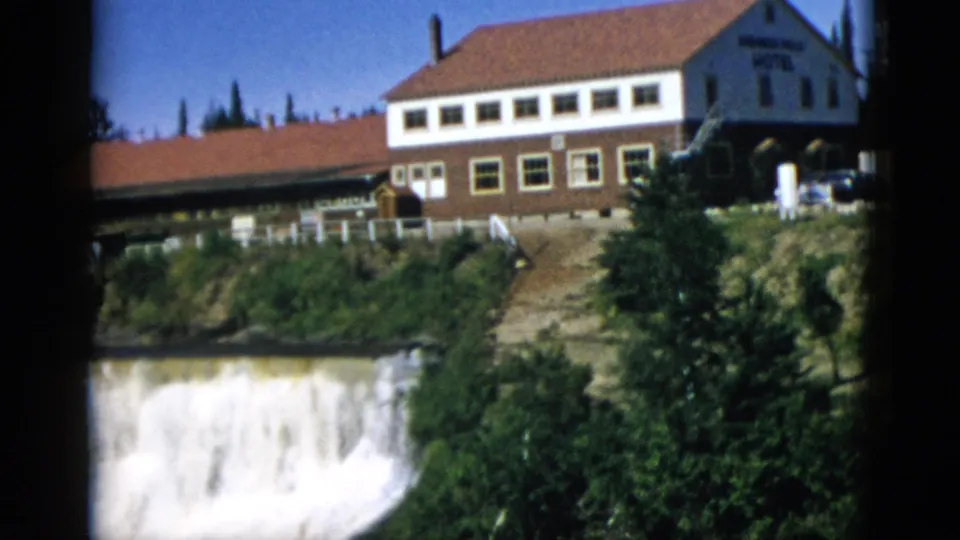 Two-story hotel on wooded cliff with waterfall cascade and rocky gorge wall filling lower frame, Quebec Canada circa 1952, 8mm home movie.