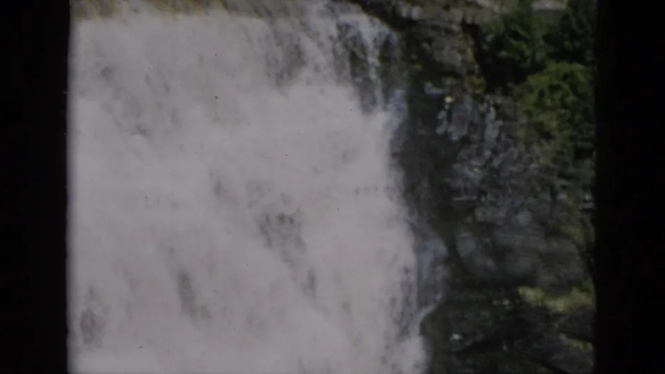 8mm home-movie close-up of cascading white water against a dark cliff, with green foliage and characteristic film borders, Quebec Canada, c.1952.