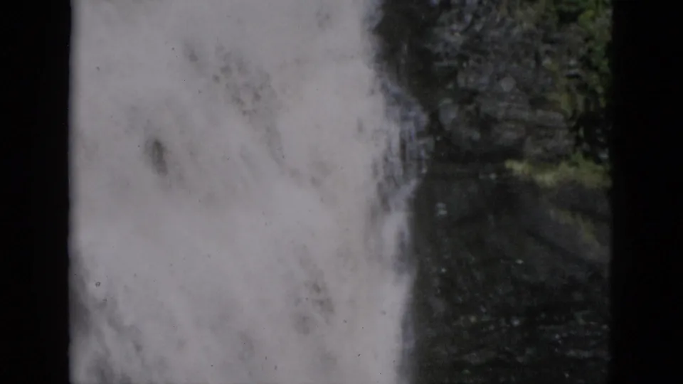 8mm film frame of a powerful waterfall in a narrow rocky gorge, green vegetation on the right, with turbulent water at the base, Quebec Canada, c.1952.