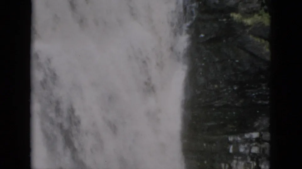 8mm home-movie frame of white water falling against a dark cliff with green foliage, characteristic film borders at edges, Quebec Canada, c.1952.