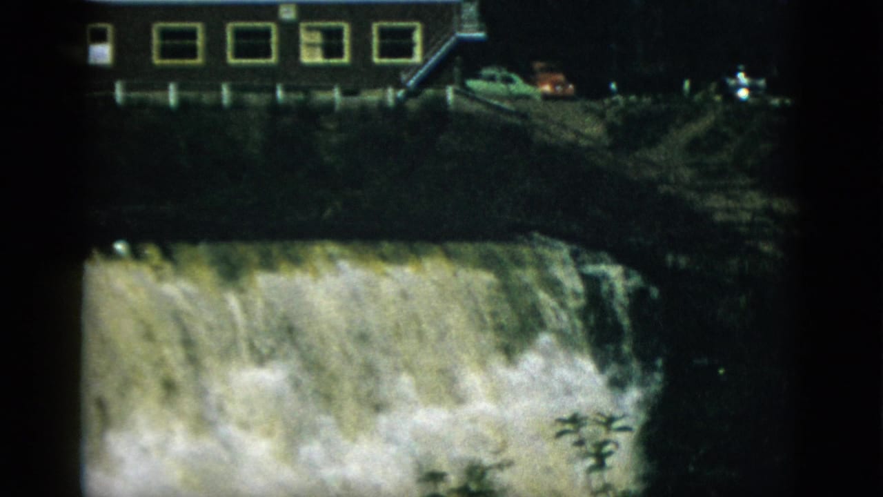 8mm home movie frame circa 1952, Quebec, Canada — massive waterfall or dam spillway with a long-windowed building and period cars on the embankment above.