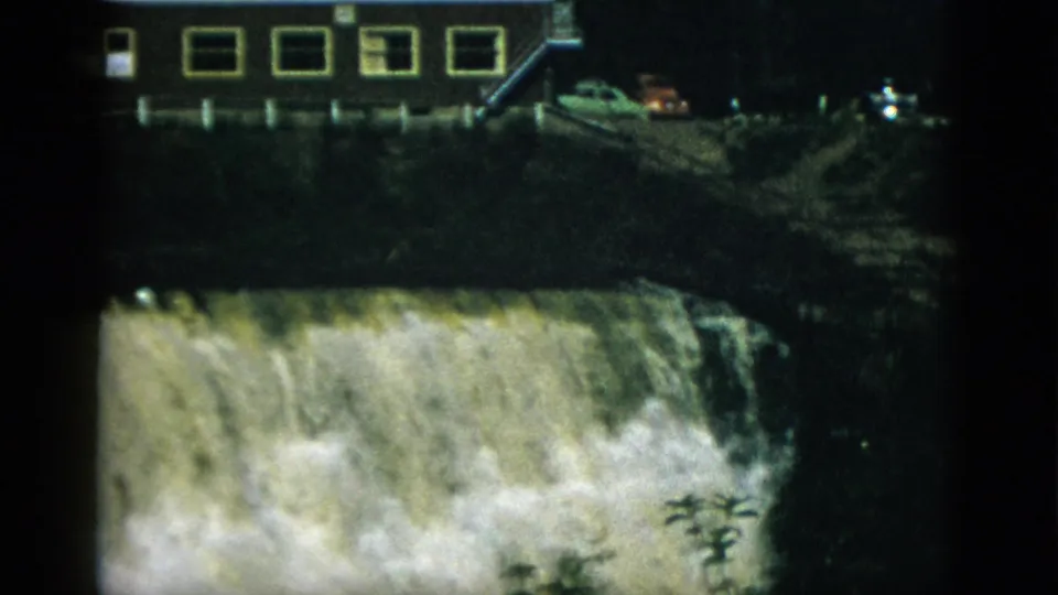 8mm home movie frame circa 1952, Quebec, Canada — massive waterfall or dam spillway with a long-windowed building and period cars on the embankment above.