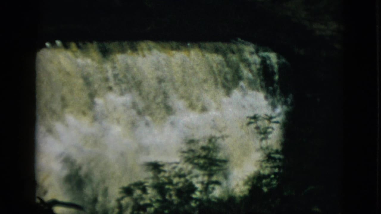 A large cascading waterfall with white turbulent water and dark tree silhouettes in the lower frame, on 8mm film.