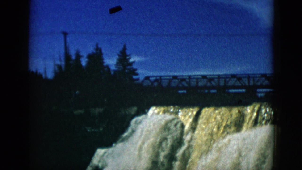 1952 Quebec — 8mm home movie of a dam waterfall with amber-toned cascading water, white frothy rapids, and metal truss bridge above against a deep blue sky.