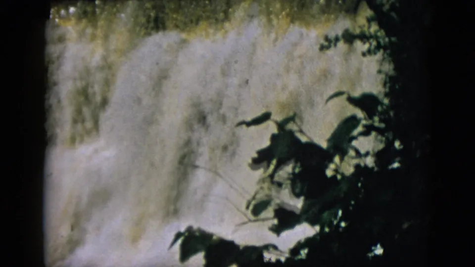 8mm film circa 1952, Quebec waterfall with denser deciduous foliage foreground framing and mist patches visible through branches.